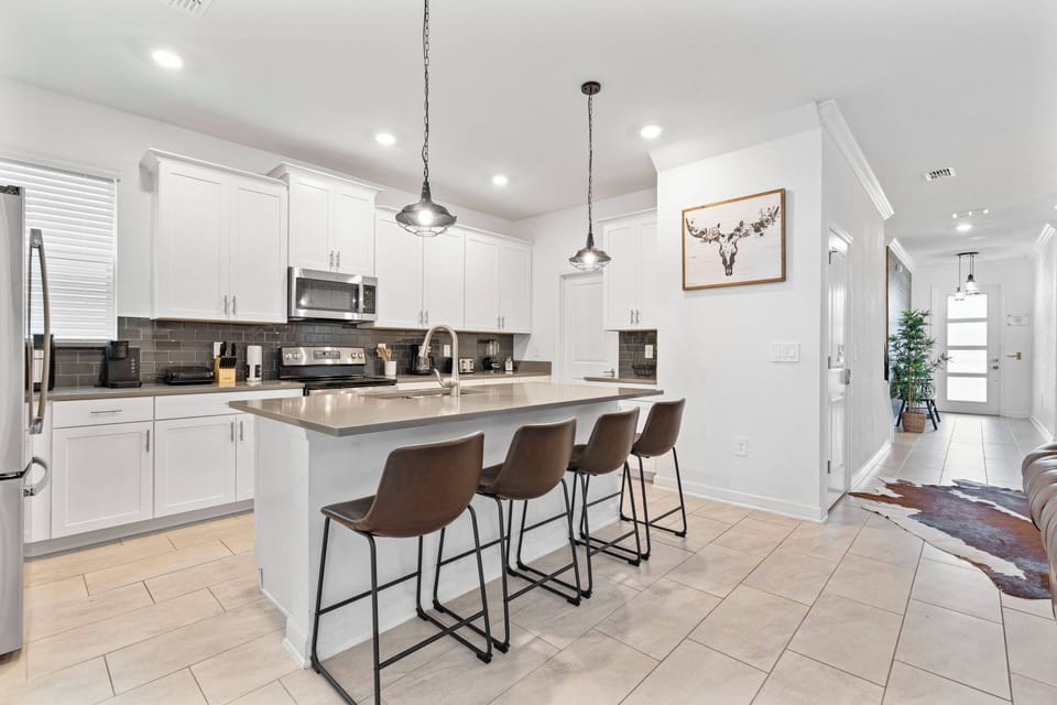 Discover the heart of your stay in this stylish kitchen with sleek white cabinetry and a spacious island ideal for casual meals. Warm wood stools add a cozy touch, making it a perfect spot to gather and unwind.
