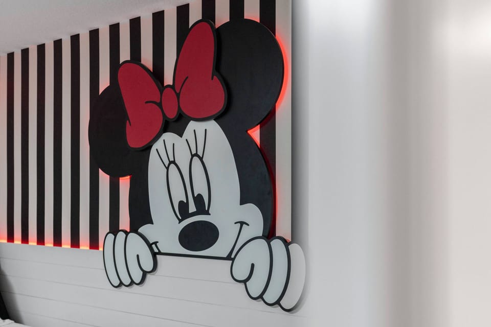 Enjoy the playful charm of this room, featuring a vibrant Minnie Mouse mural set against bold black and white stripes. The soft ambient lighting adds to the whimsical decor, creating a delightful atmosphere for guests of all ages.