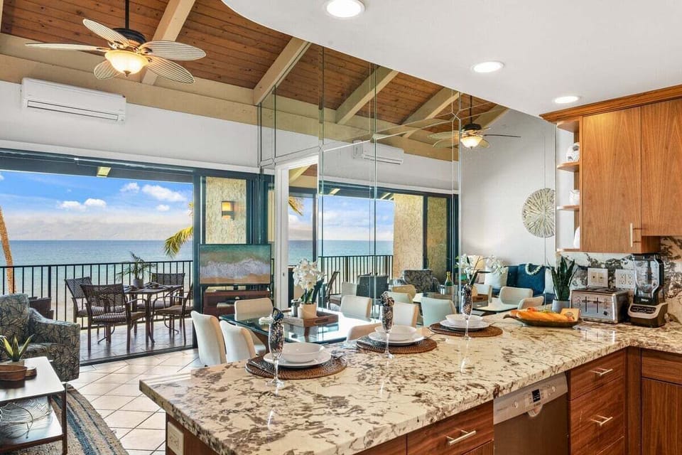 A dining space with ocean views just beyond the balcony, framed by vaulted ceilings and natural light.