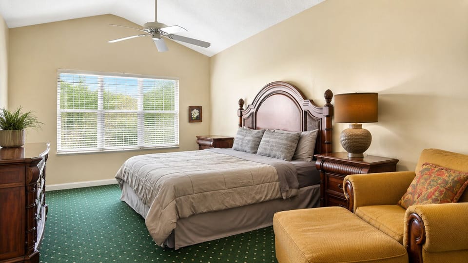 Bright bedroom featuring a large bed, ceiling fan, seating area, and natural light from the window.