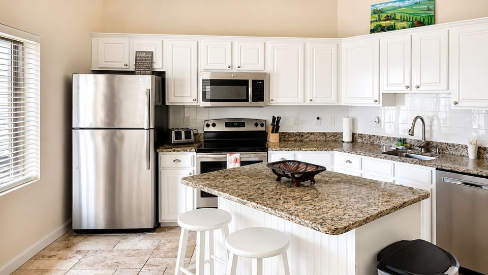Bright kitchen with white cabinetry, stainless steel appliances, granite counters, and breakfast bar seating.
