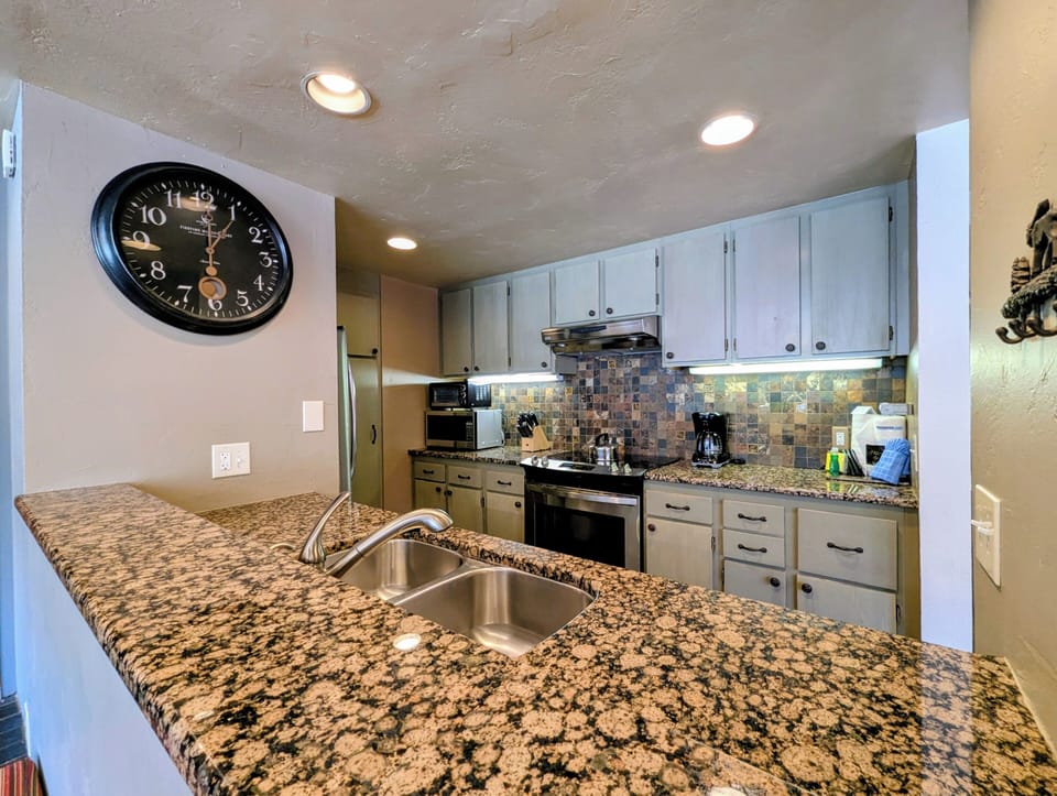 Fully equipped kitchen with granite countertops, modern appliances, and colorful tiled backsplash—your home base for cooking memorable vacation meals.