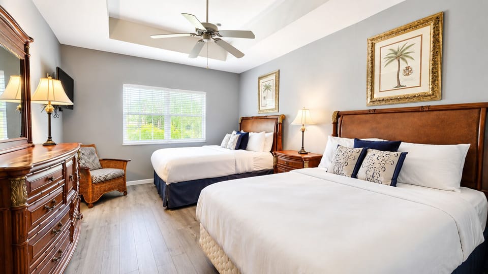 Bright bedroom with two comfortable beds, dresser storage, ceiling fan, and warm natural light.