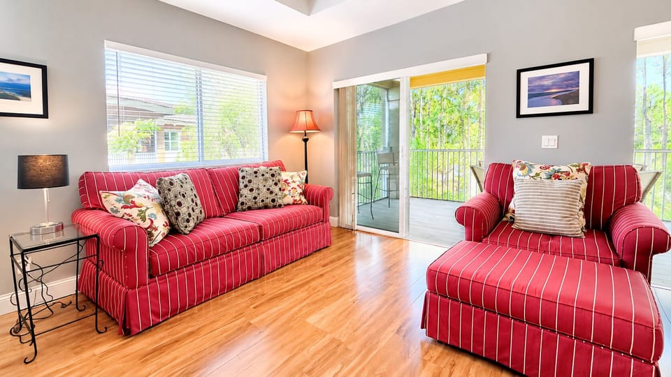 Comfortable living area featuring red sofa seating, wood-look flooring, large windows, and access to the screened balcony.