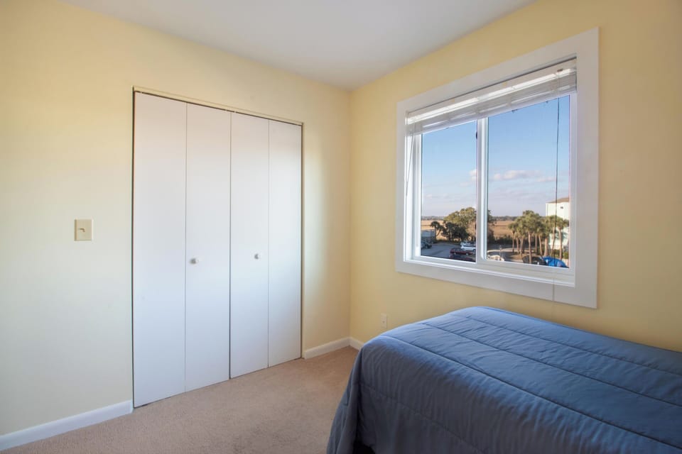 Your cozy bedroom features generous closet space and a bright window offering peaceful views of palm trees and distant landscapes.