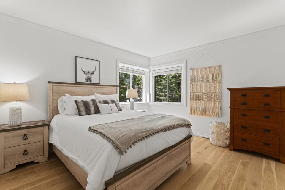 Sunlit bedroom w/ corner windows, wood furniture & peaceful tree views