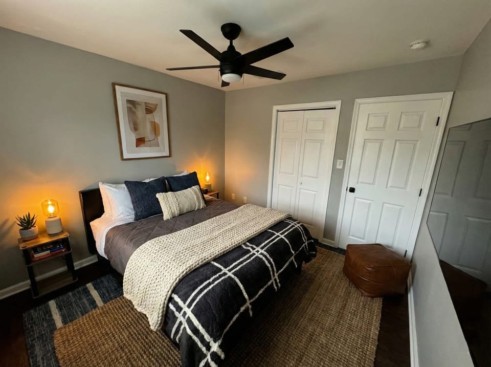 Bedroom with made bed, ceiling fan, bedside lighting, and closet doors.