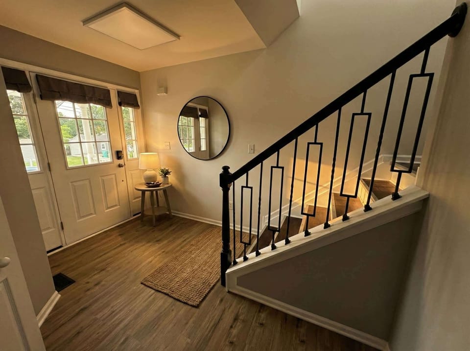 Entryway with staircase, front door, mirror, and small seating area.