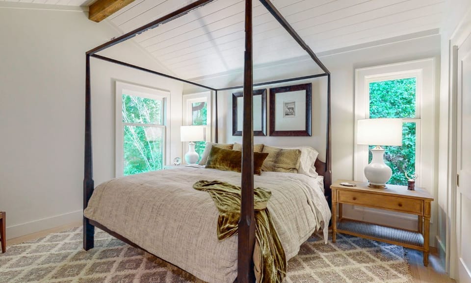 Cozy bedroom with a dark wood canopy bed and natural light from three windows