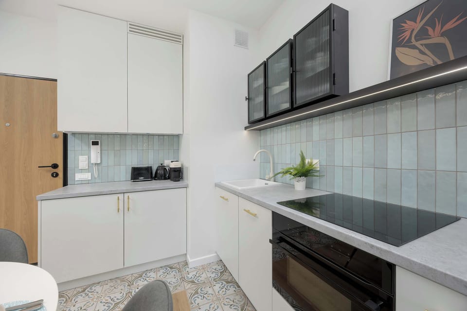 A minimalist kitchen with white cabinetry, black upper units, and a patterned rug underfoot.

