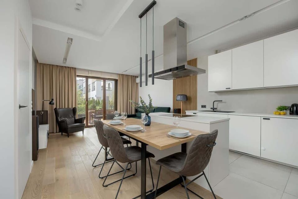 A modern dining area with a kitchenette, elegant table, and ceiling lights creates a perfect space for spending time together.