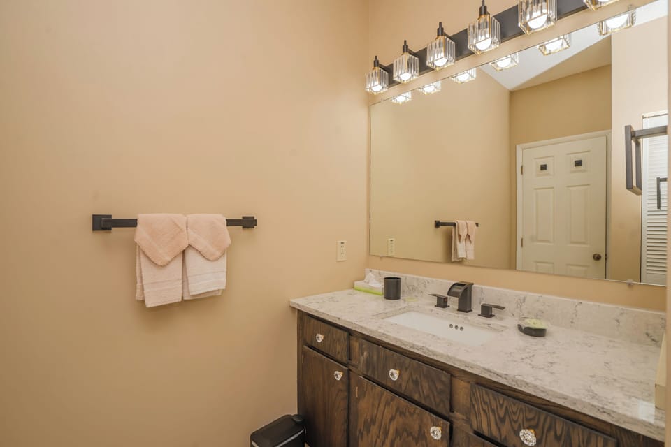 Step into your serene bathroom retreat with marble counters, warm wood cabinetry, and plush pink towels ready for your stay.