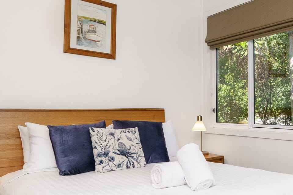 Queen-size bed with professionally laundered linen, ensuring a comfortable and restful stay, complemented by large windows showcasing lush greenery for a serene and refreshing ambiance.
