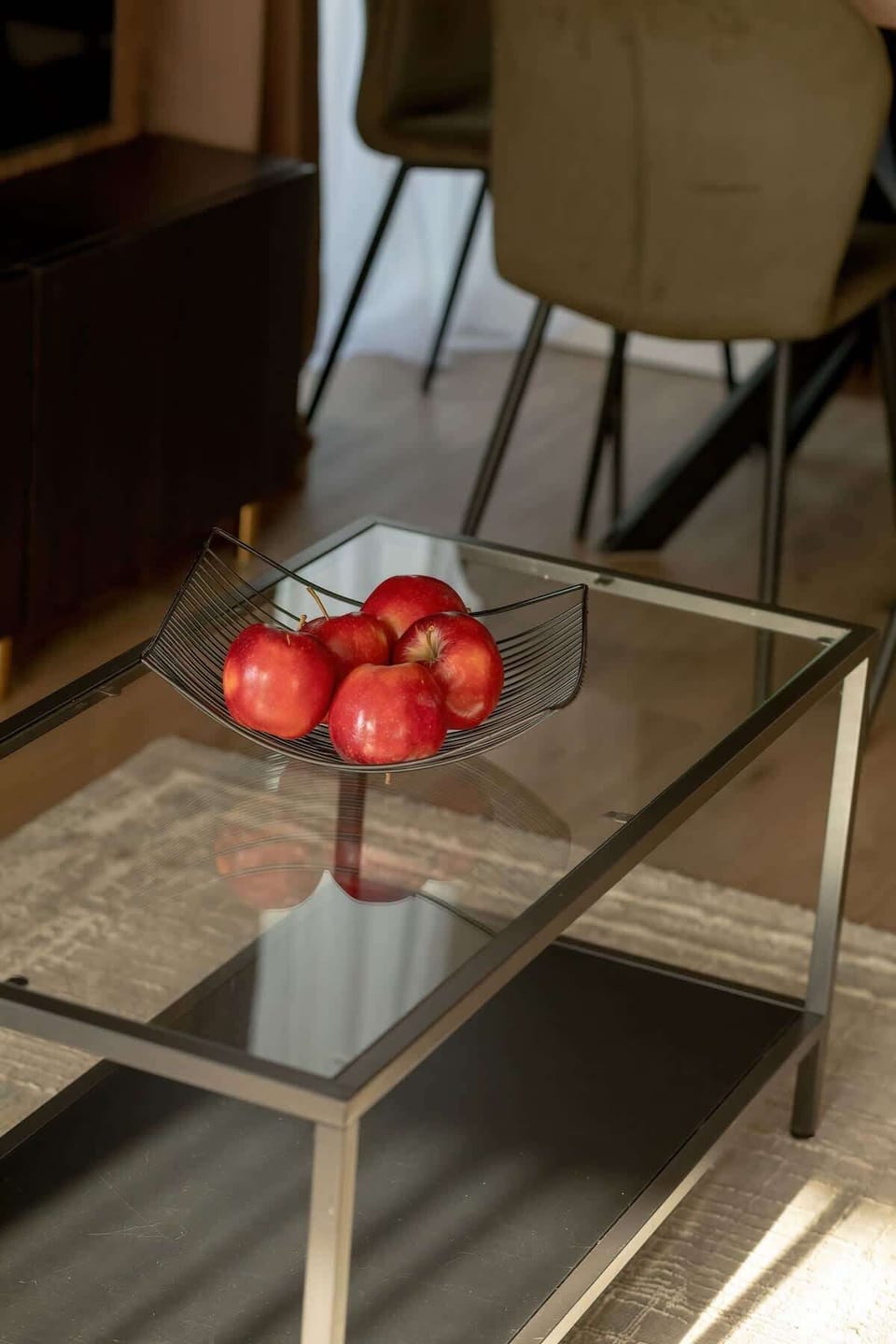 A glass coffee table with a metal frame, placed on a rug and decorated with a bowl of red apples, adds an elegant and cozy touch to the dining area.