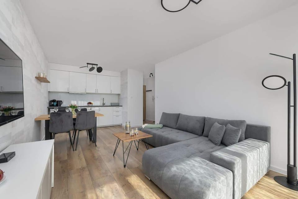 A modern living room with a gray sectional sofa, wooden flooring, and an open kitchenette creates a perfect space for relaxing and cooking.