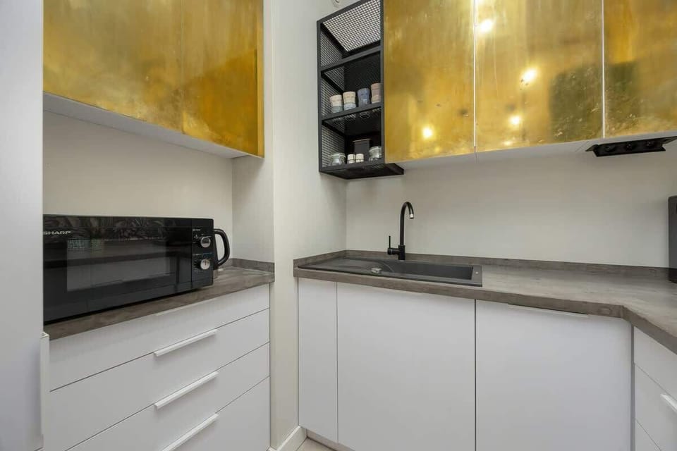 A modern kitchenette with elegant golden cabinets, black fixtures, and a microwave offers a stylish and functional space for preparing meals.