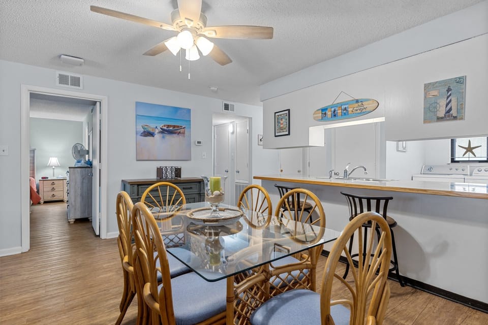 Your coastal-themed dining room features a glass table surrounded by wicker chairs, perfect for family meals with beachy artwork setting the mood.