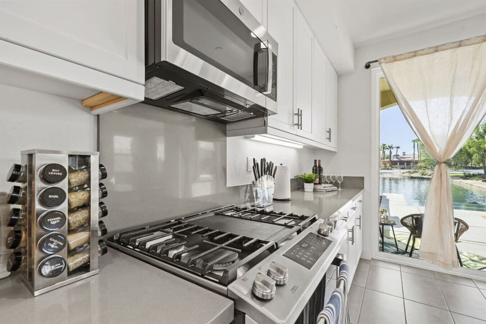 Well-equipped kitchen for culinary adventures featuring a stainless steel stove, spice rack, and a pool view in the backyard.