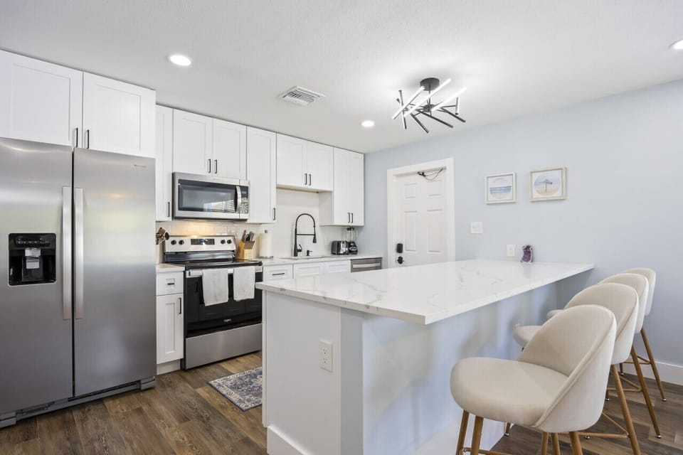 Cocoa Beach Kitchen | Bright seaside space featuring a waterfall island, coastal artwork, and soft blue design accents