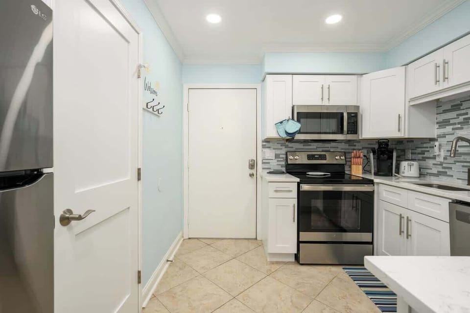 Bright coastal kitchen in soft blue with full appliances, and a mosaic backsplash