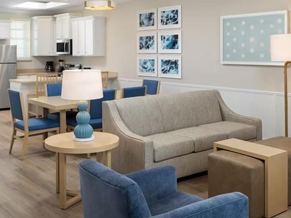 Beige sofa and blue armchairs in the open living area with dining table and blue chairs — artwork on the walls