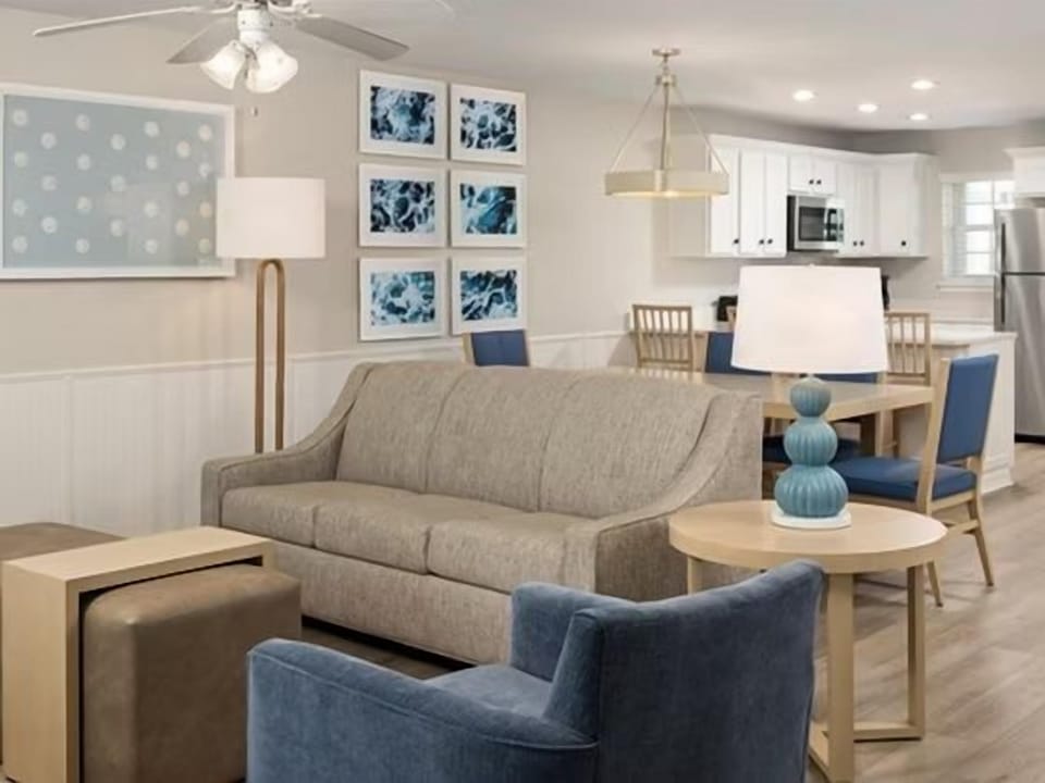 Beige sofa, blue armchairs, and wooden coffee table in the living area — kitchen visible in the background
