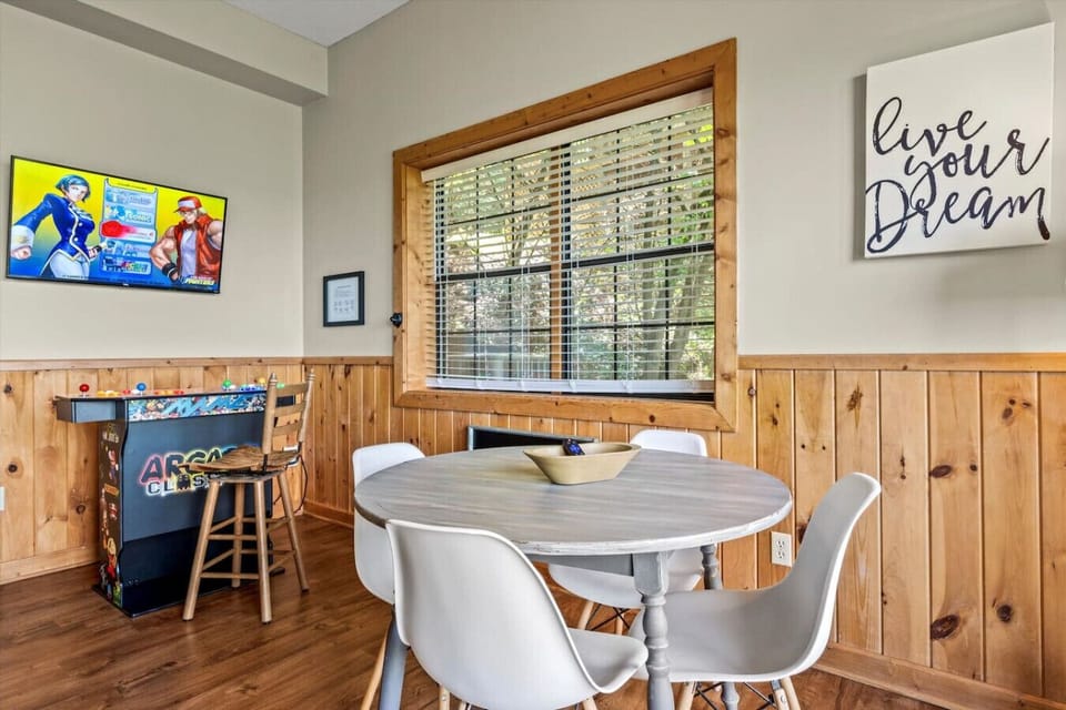 The game room includes a table for board games or cards and there is a multi-cade arcade setup.