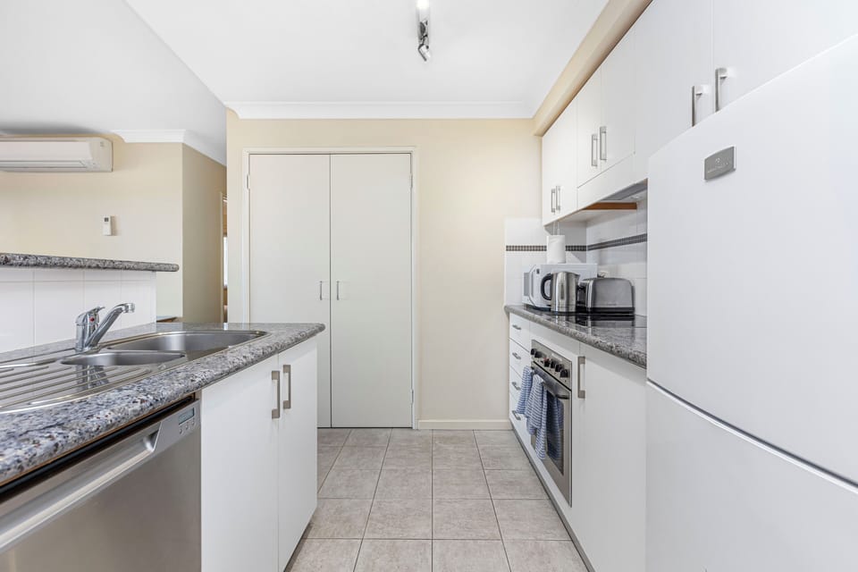 Our practical galley kitchen features sleek white cabinets, durable stone countertops, and stainless steel appliances including a dishwasher. Perfect for easy meal prep!