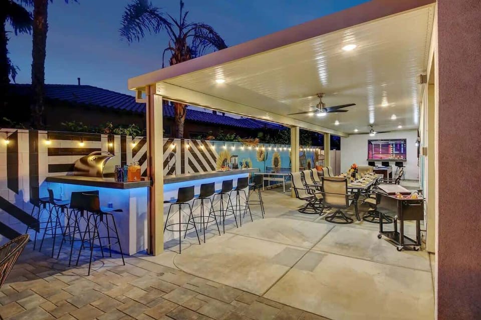 Sip and unwind at the covered outdoor bar with stools, ceiling fans, and TV entertainment.