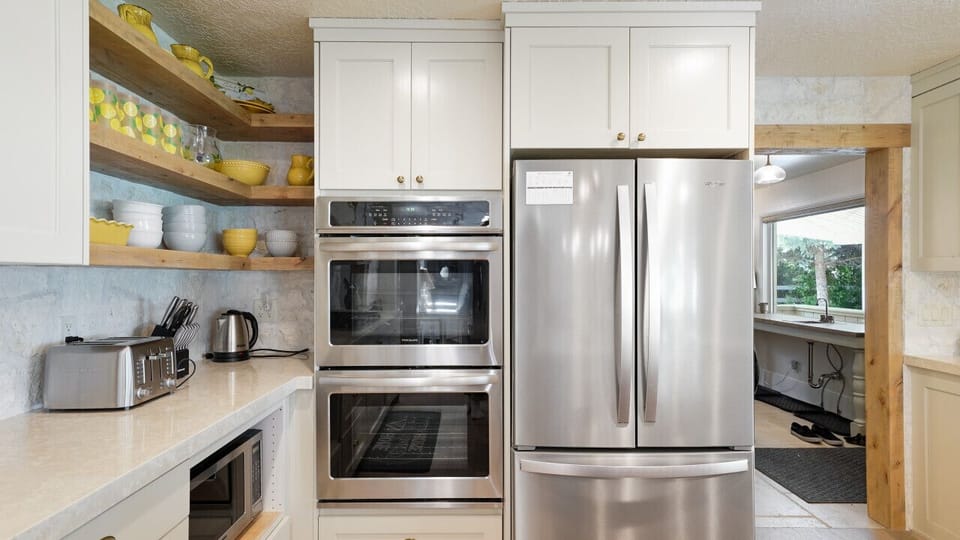 A kitchen full of character: yellow porcelain ware pops against white and wood cabinetry, with the oven, toaster, microwave, and fridge ready for action.
