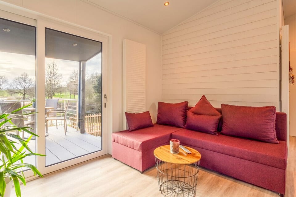 Bright living room w/ a plush red sofa & warm natural light streaming through large windows.