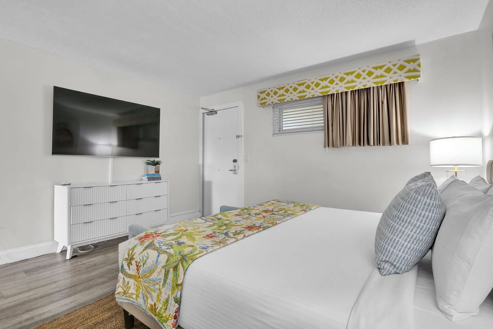 Relax in your bright, modern bedroom featuring a comfortable king bed with tropical-inspired linens, flat-screen TV, and stylish furnishings for the perfect getaway.