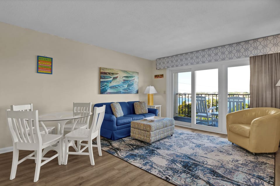 Your bright living space combines comfort with coastal charm, featuring a cozy blue sofa and dining area perfect for relaxing after beach days.