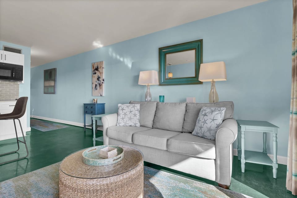 Sink into your plush gray sofa surrounded by soothing blues and greens, where modern comfort meets coastal charm in your stylish retreat.