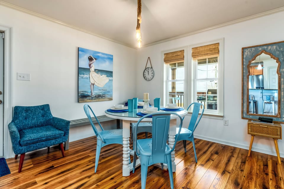 Gather around your bright dining table with coastal-inspired blue chairs, where morning coffee and evening meals feel extra special beneath the warm rope lighting.