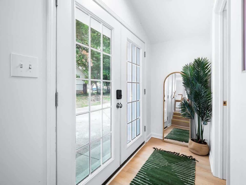 - Entryway with glass doors allowing natural light to flow inside   - Full-length mirror and indoor greenery create a warm welcome   - Perfect Airbnb entry offering charm and a fresh atmosphere  