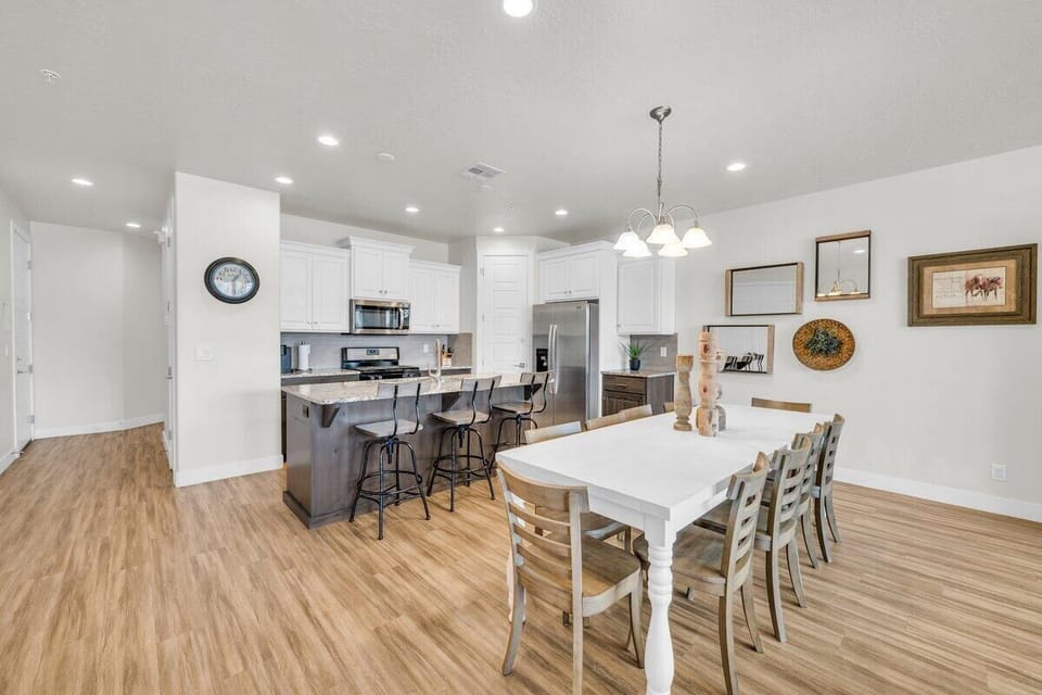 Bright open-concept kitchen and dining area in Washington UT vacation rental with stainless steel appliances, island seating, and farmhouse-style dining table.