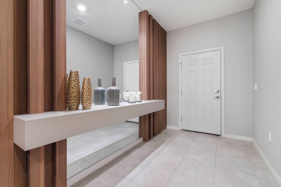Welcome to an inviting entryway with sleek light tiles and warm wood accents that create a stylish atmosphere. Modern shelving and decorative vases add sophistication and charm to this beautifully designed space.