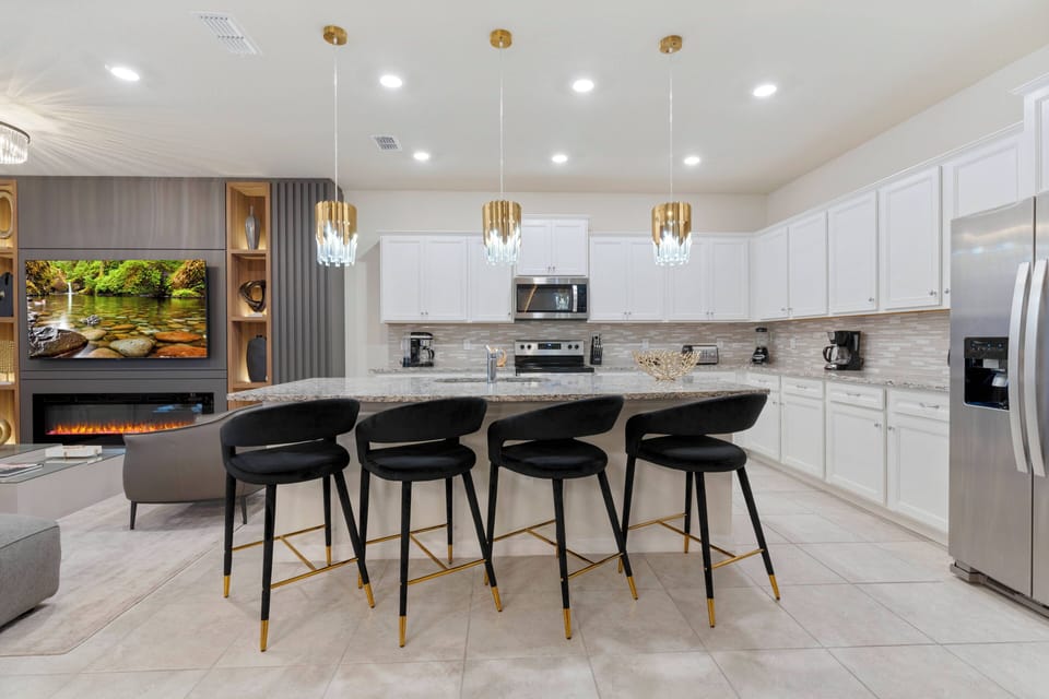Come together at the sleek marble island, where chic black bar stools offer a perfect spot for dining and conversation. The bright white cabinetry and cozy lighting create a welcoming space for meals or your morning coffee.