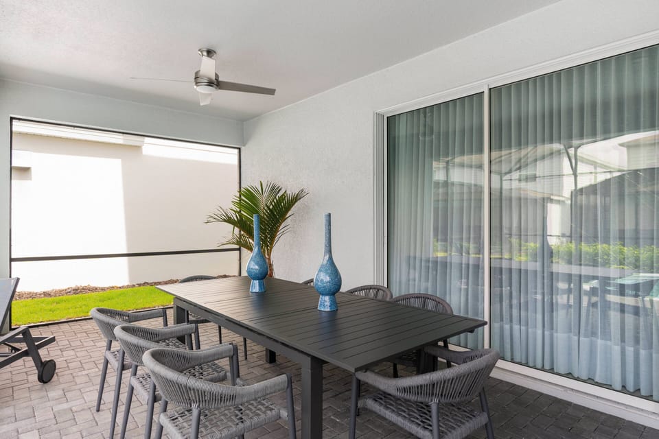 Step outside to a spacious dining area ideal for alfresco meals, complete with a sleek black table, comfy chairs, and vibrant blue vases that enhance the atmosphere.