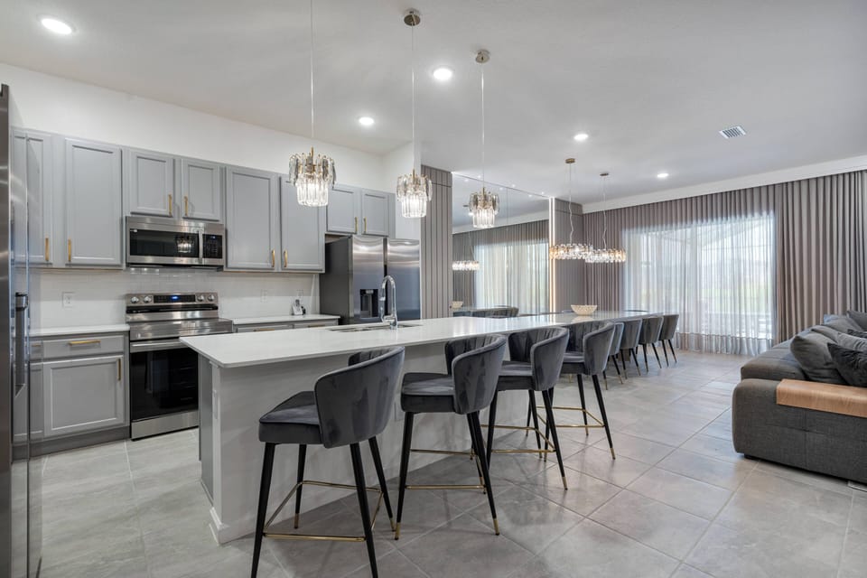 This bright, airy kitchen features modern gray cabinetry and stainless steel appliances, making meal prep enjoyable. The spacious island with stylish stools is perfect for casual dining and gathering with friends and family.