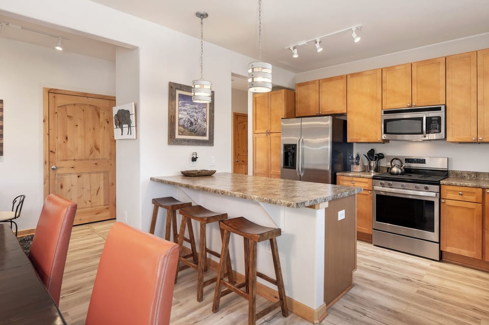 - Fully equipped kitchen with stainless steel appliances and spacious island bar - Three wooden stools make it easy to gather for snacks or morning coffee - Pendant lights and wood cabinetry create a warm, polished atmosphere