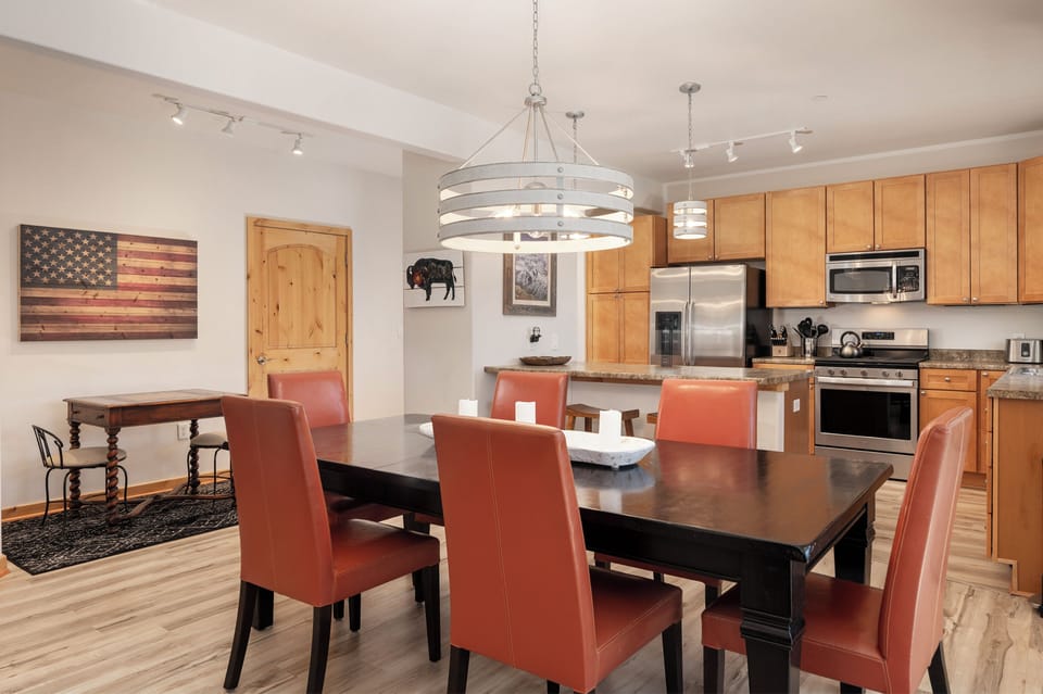 - Spacious dining area with seating for six in bold orange leather style chairs - Large wood table perfect for meals, board games, or group gatherings - Open layout connects seamlessly to the kitchen and living room beyond