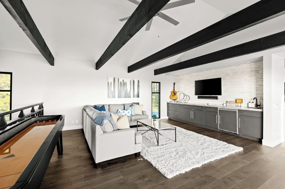 Upstairs loft with comfortable sectional, bar with beverage fridge, shuffleboard, and sliding glass doors that open to deck with seating