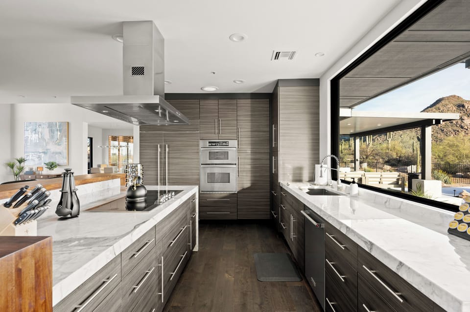 Fully stocked kitchen with barstool seating on a custom wood bar top, marble waterfall island, and stainless steel appliances