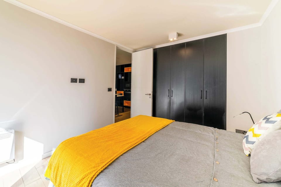 Private bedroom with a mustard-yellow textured throw, patterned accent pillow, and a full wall of matte-black wardrobes for convenient storage.