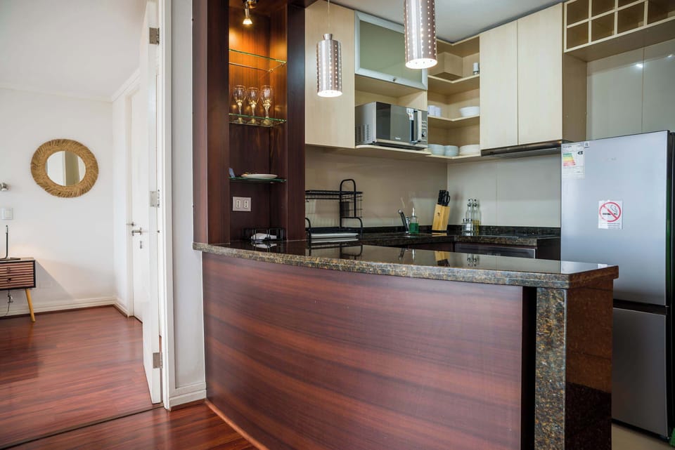Private studio kitchen with polished granite counters, pendant lighting, full-size refrigerator, microwave, and neatly arranged dishware.