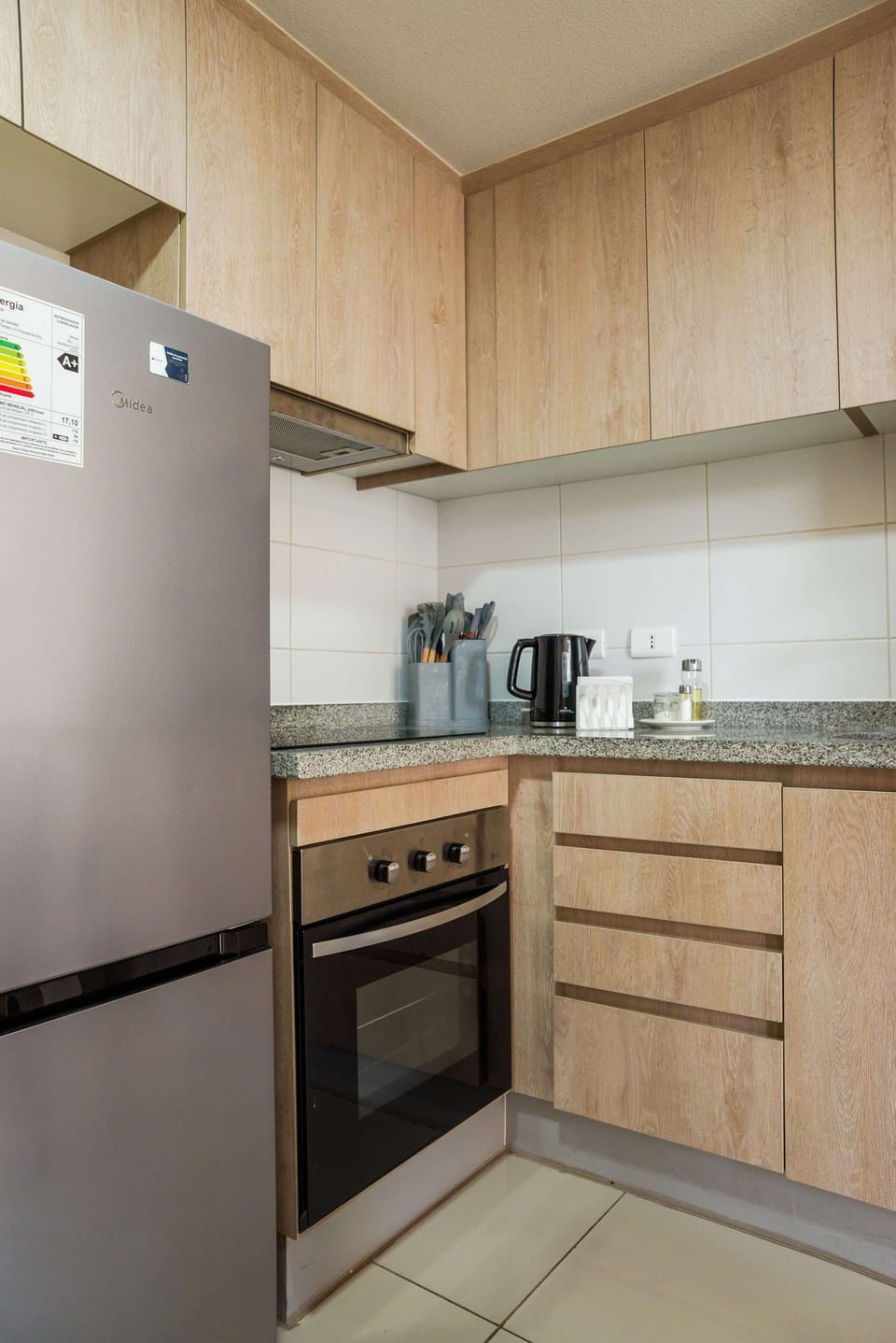 Private kitchen with light oak cabinetry, granite countertops, a full-size refrigerator, and an oven for convenient in-home cooking.