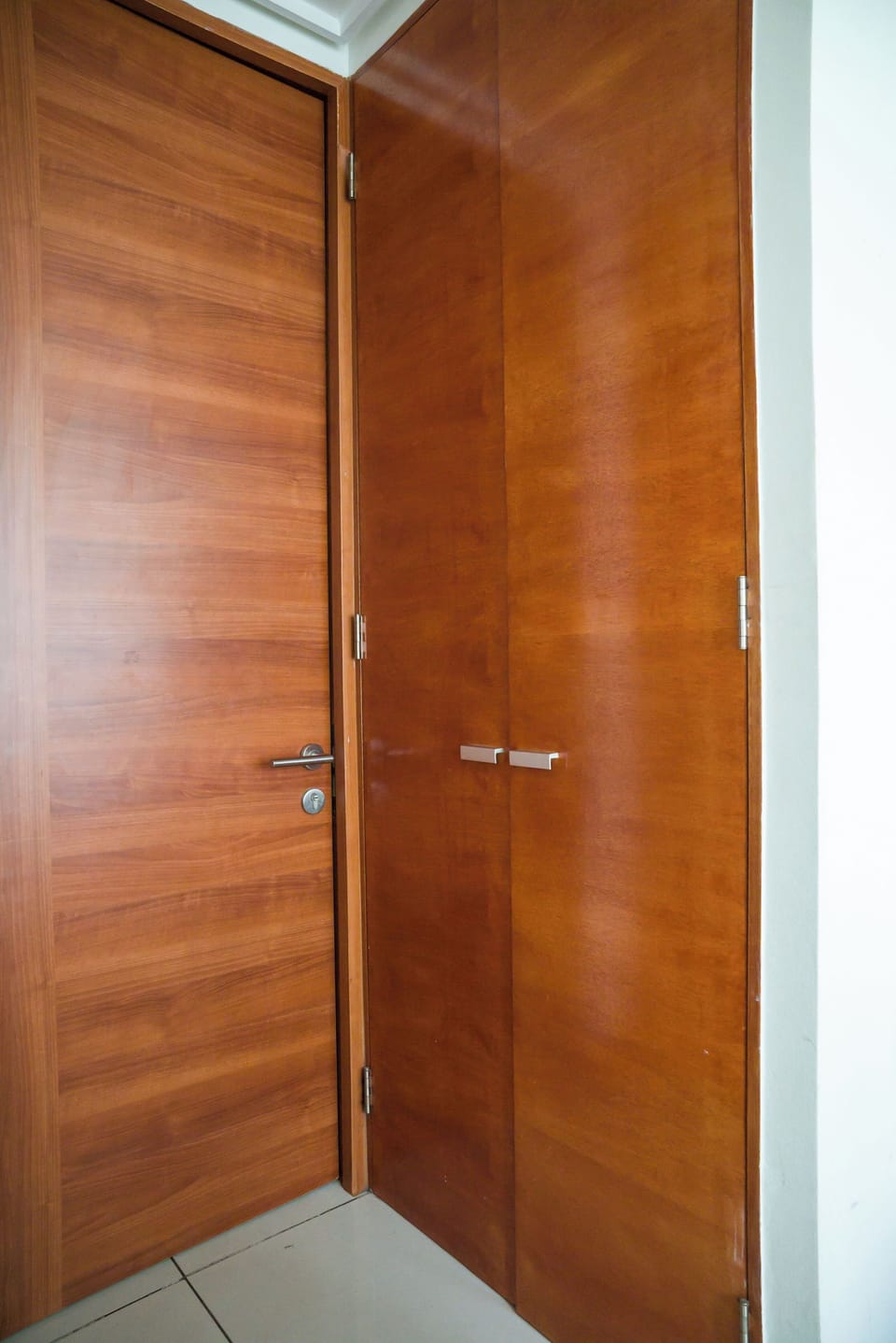 Private entrance with warm wood doors, a secure deadbolt, and light tiled flooring.