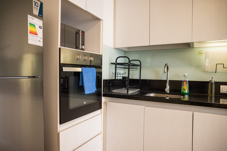 Private kitchen with built-in oven, stainless refrigerator, black granite counters, and a pale aqua glass backsplash.